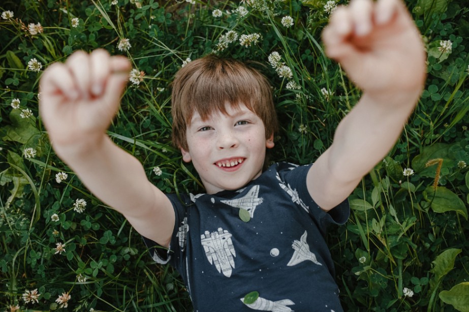 A young boy lying in a field of clover, arms stretched wide, laughing freely outdoors.