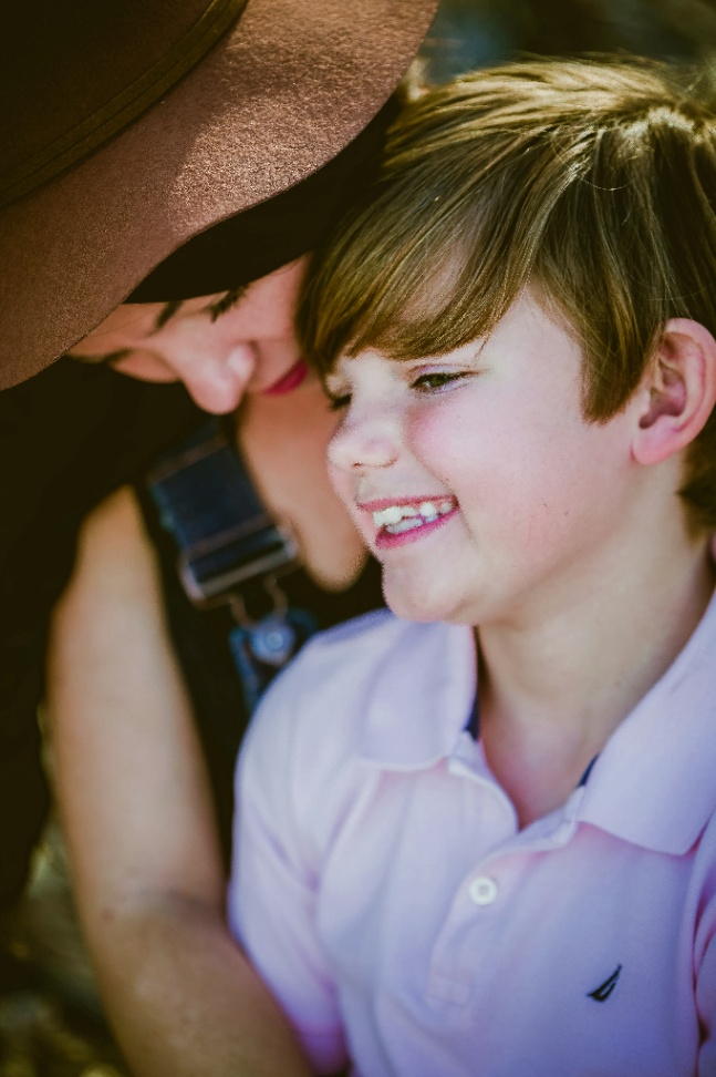 A mother leaning close to her laughing son outdoors, the warmth between them natural and unposed.